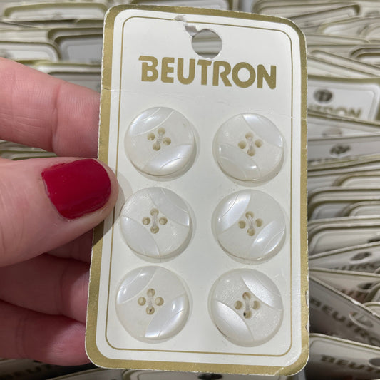 Card with white buttons held by a hand with red nail polish, with 'Beutron' branding.