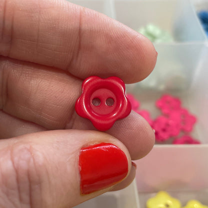 Hand holding a red button with a container of colorful buttons in the background