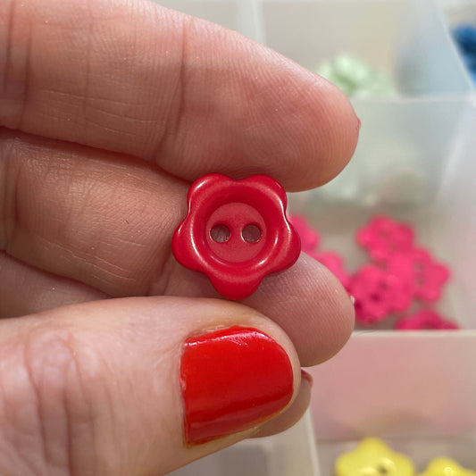 Hand holding a red button with a container of colorful buttons in the background