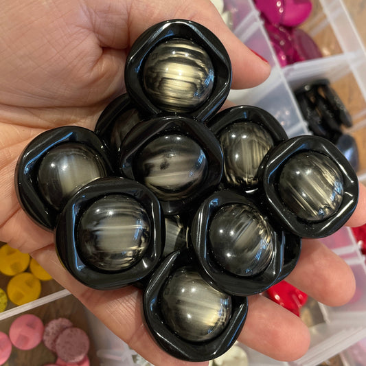 Hand holding black spherical objects with a background of colorful buttons in clear containers.