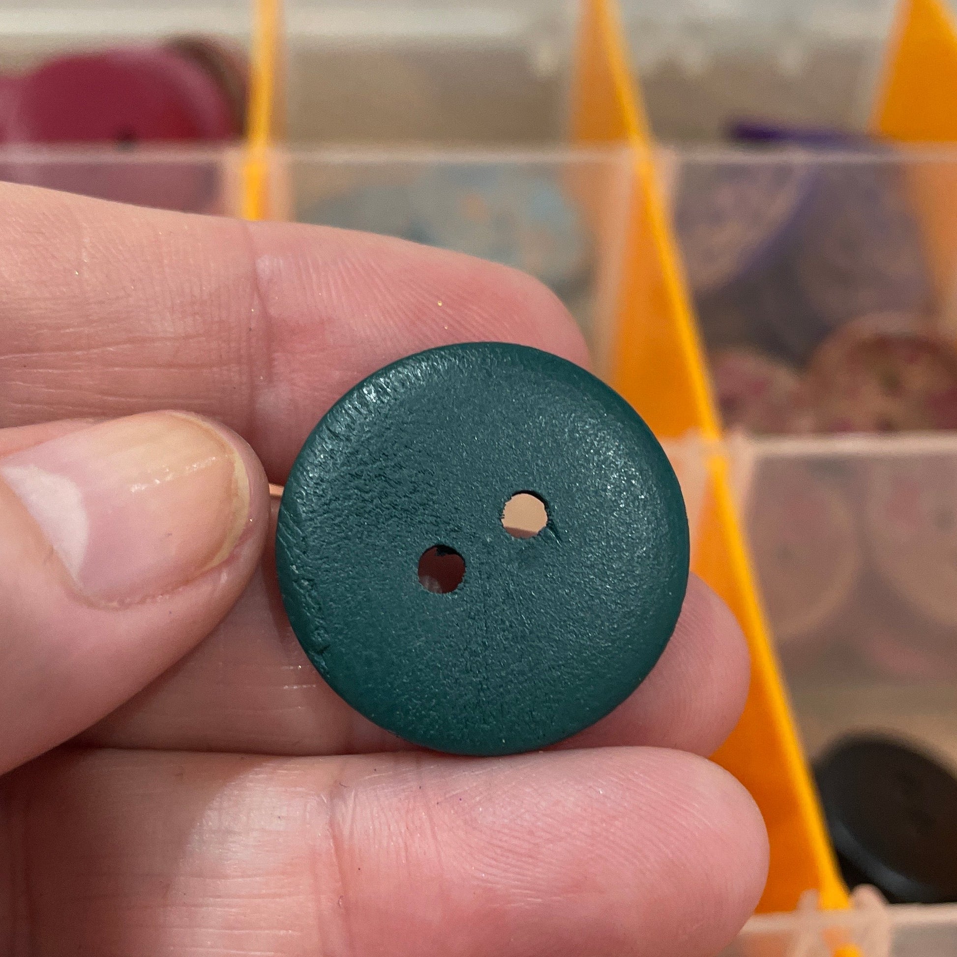 Hand holding a blue button with a blurred background of button assortment
