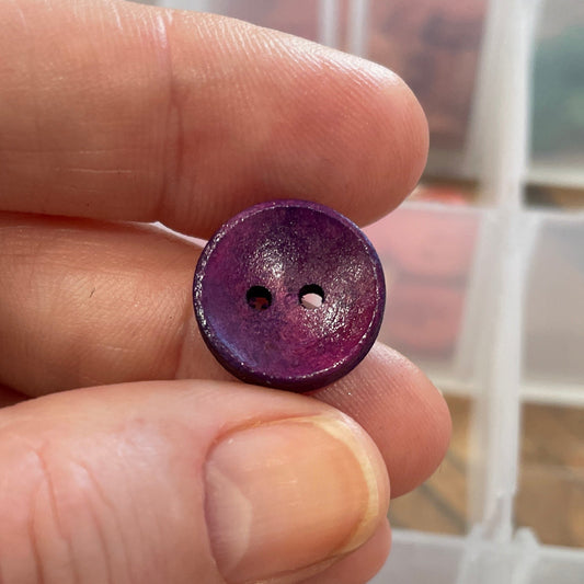 Hand holding a purple button with a container of buttons in the background