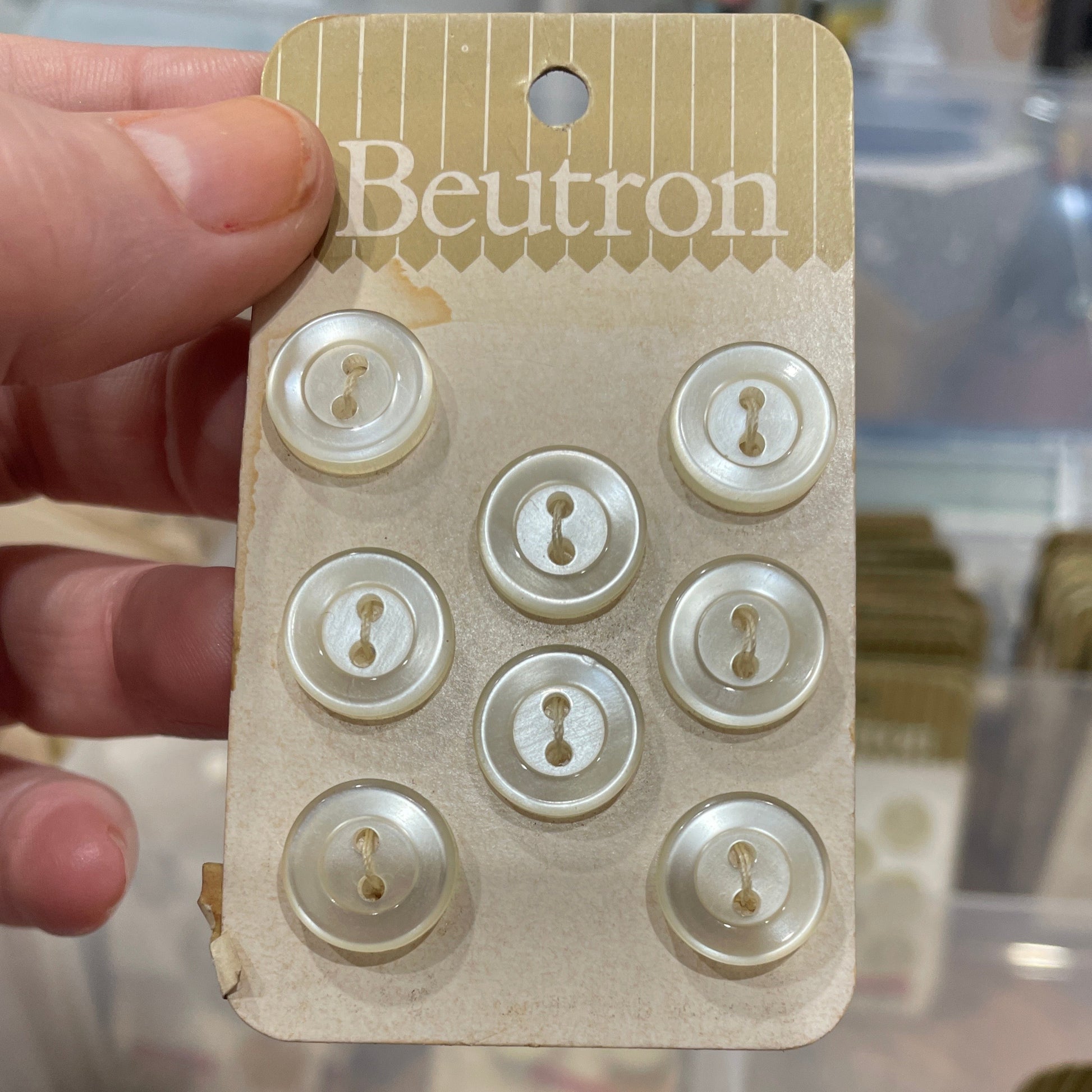 Beutron button card held by a hand against a blurred background.