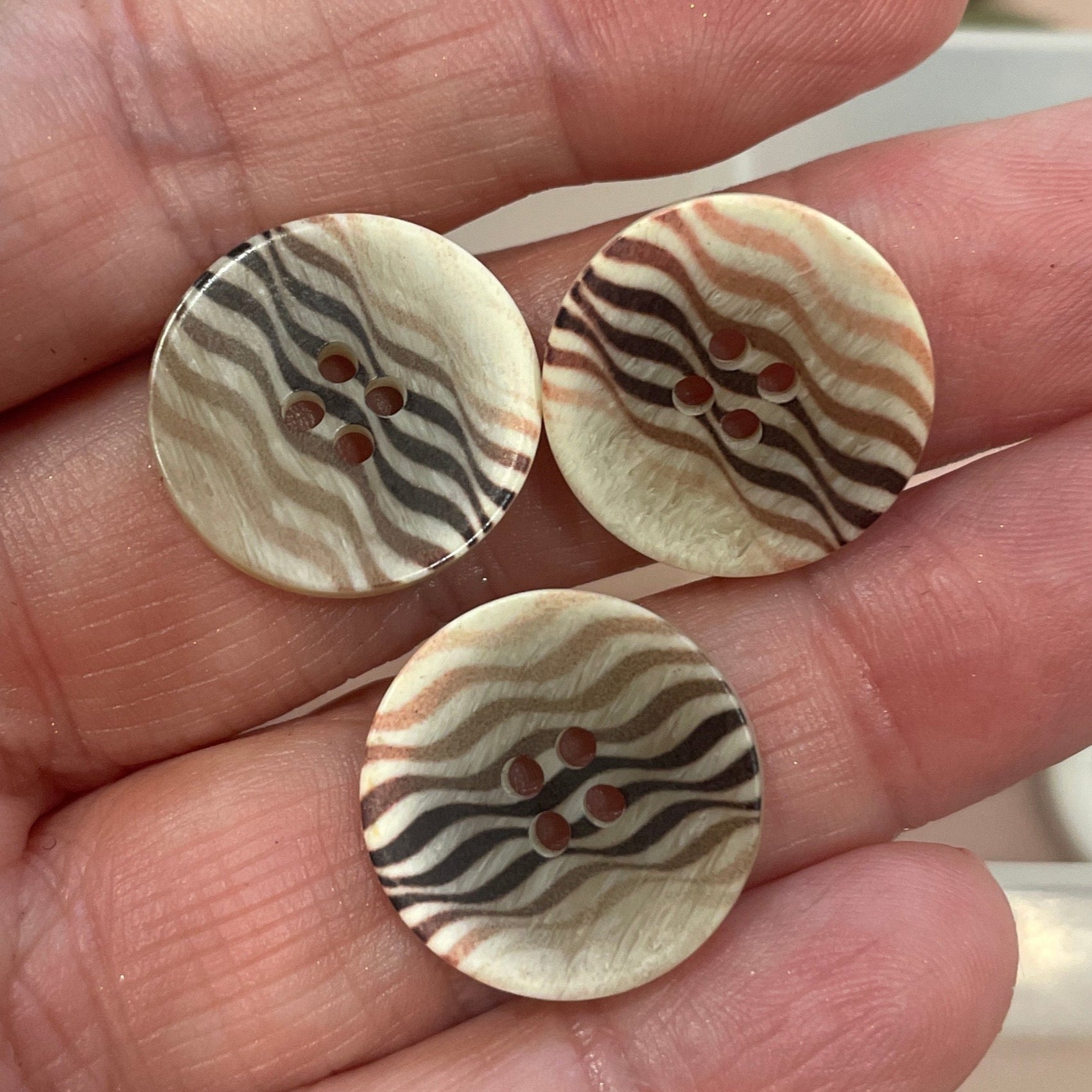 Three decorative buttons held in a hand with a button collection in the background.