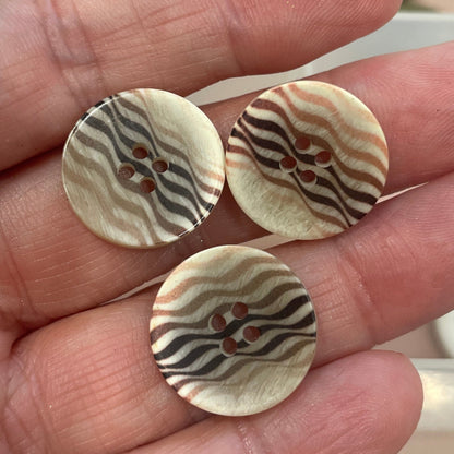 Three decorative buttons held in a hand with a button collection in the background.