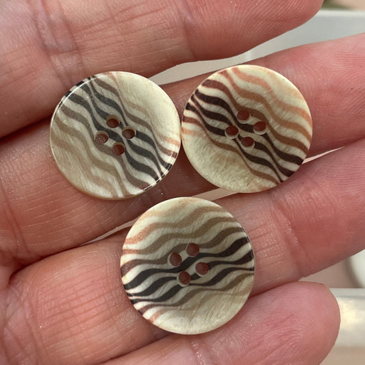 Three decorative buttons held in a hand with a button collection in the background.