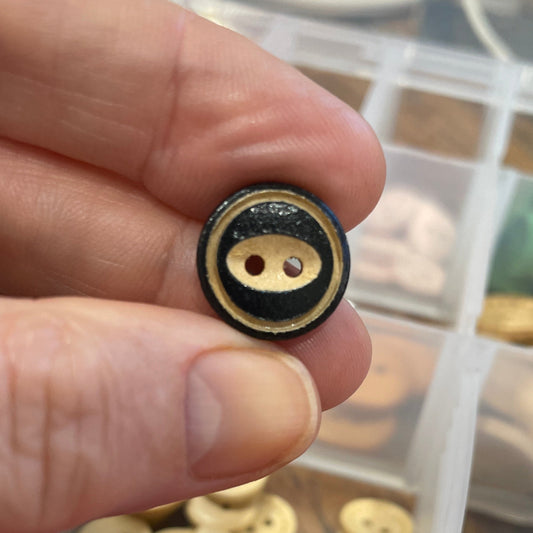 Hand holding a gold button with a container of colorful buttons in the background