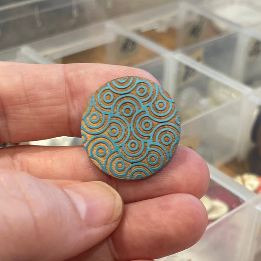 Hand holding a decorative button with a container of buttons in the background