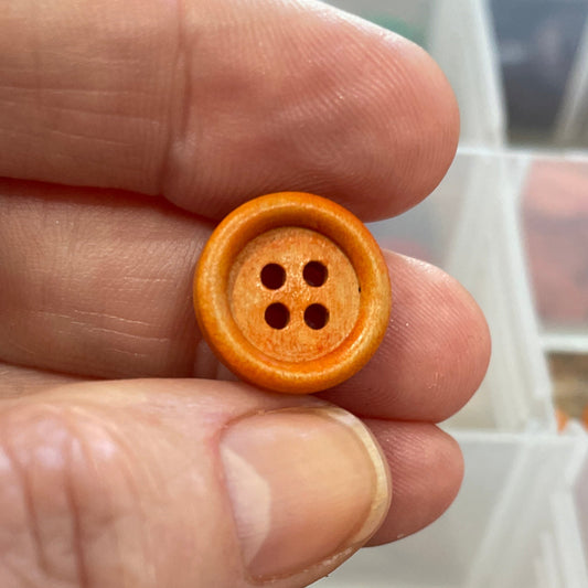 Hand holding a small wooden button with a container of colorful buttons in the background.