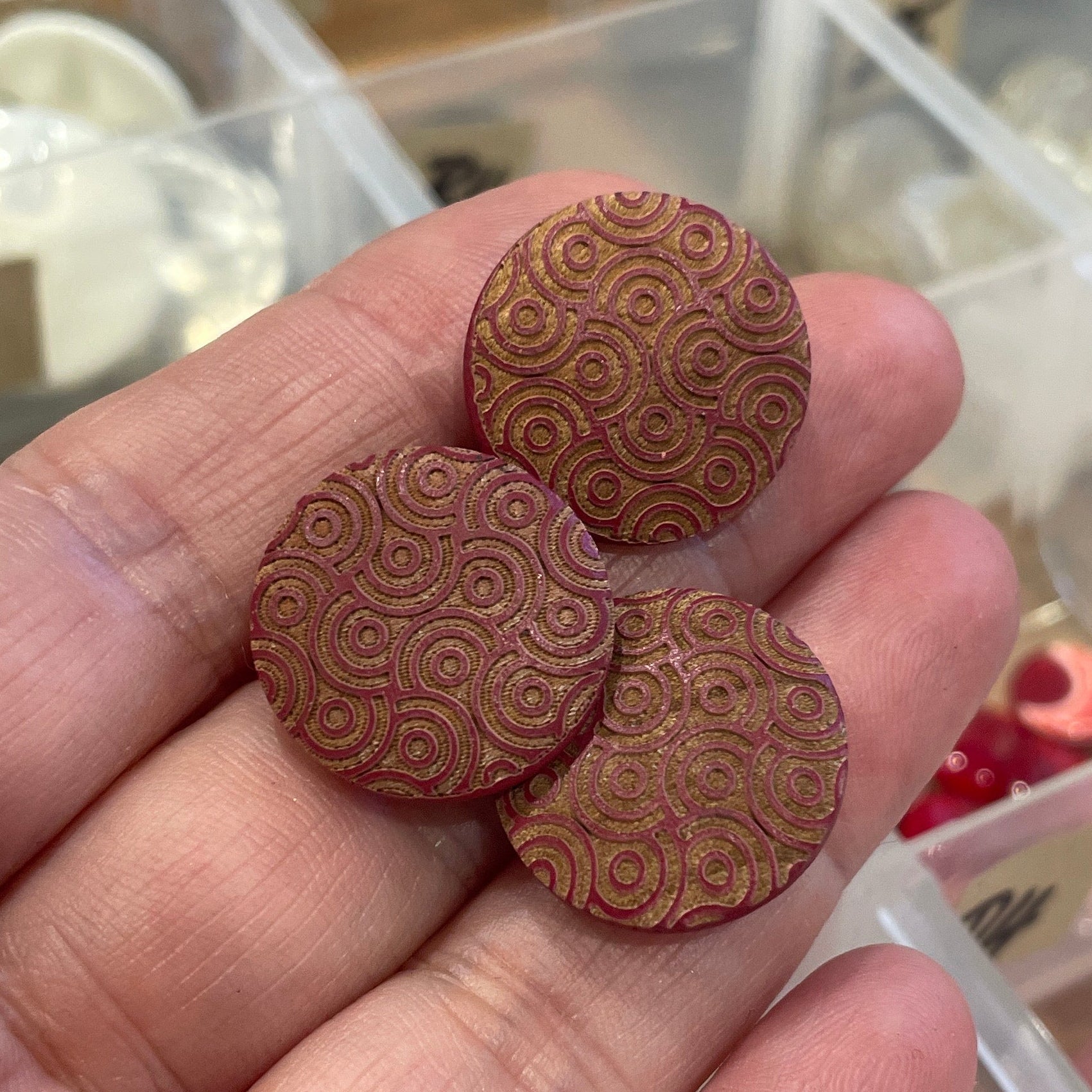 Hand holding wooden buttons with intricate patterns in front of a clear plastic organizer.