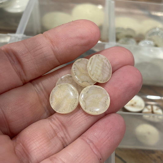 Hand holding four round, clear stones with a blurred background of a jewelry organizer.