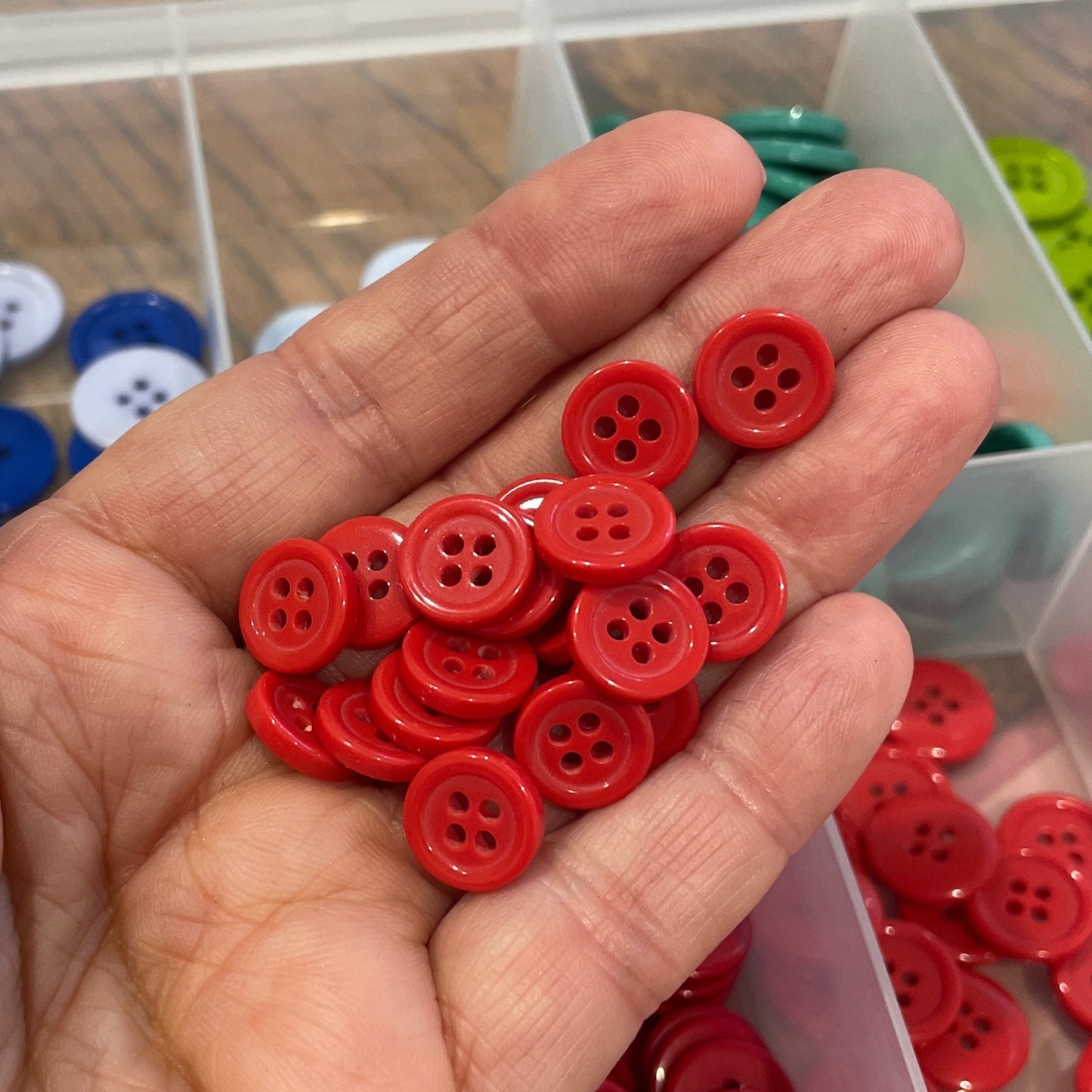 Hand holding red buttons with a clear container of buttons in the background
