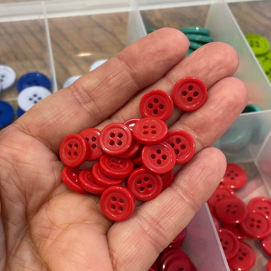 Hand holding red buttons with a clear container of buttons in the background