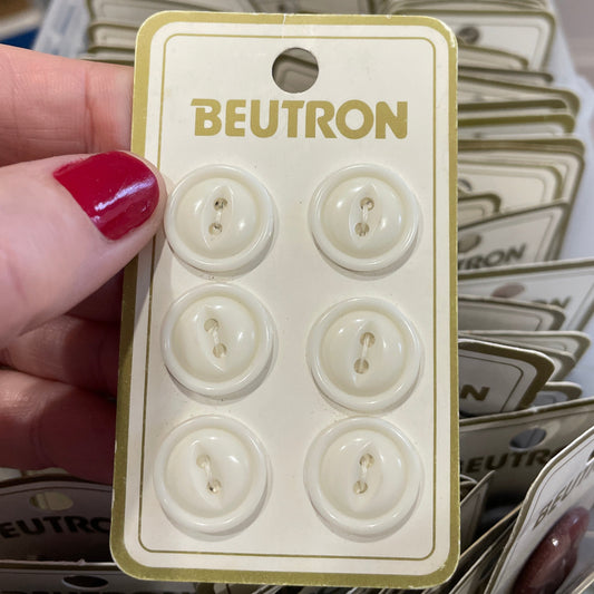 Pack of white buttons with 'Beutron' branding held by a hand.