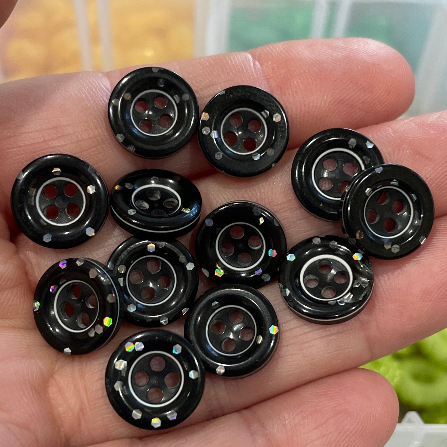 Hand holding black buttons with a blurred background of button containers.