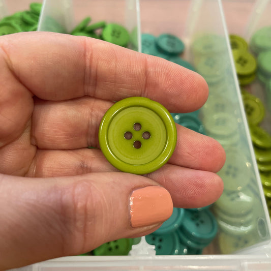 Hand holding a green button with a container of buttons in the background