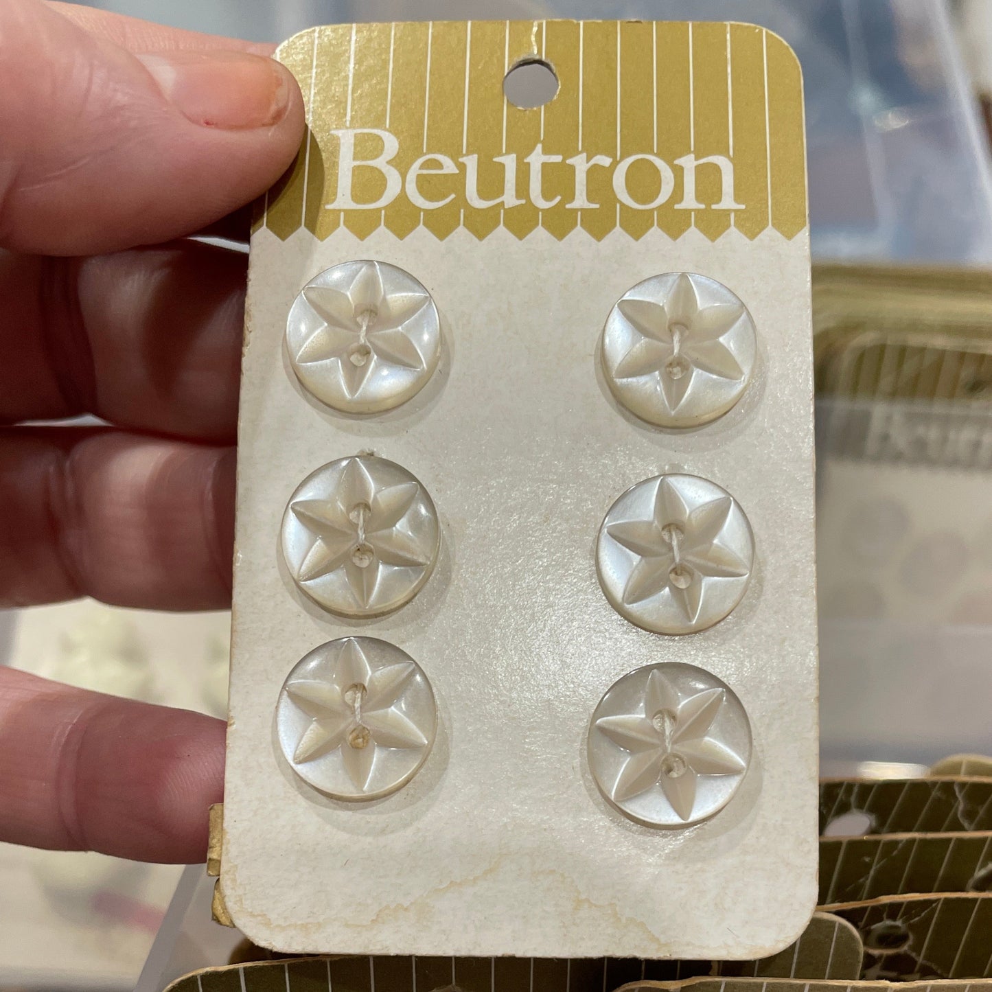Beutron buttons on a card held by a hand with a clear plastic container in the background.