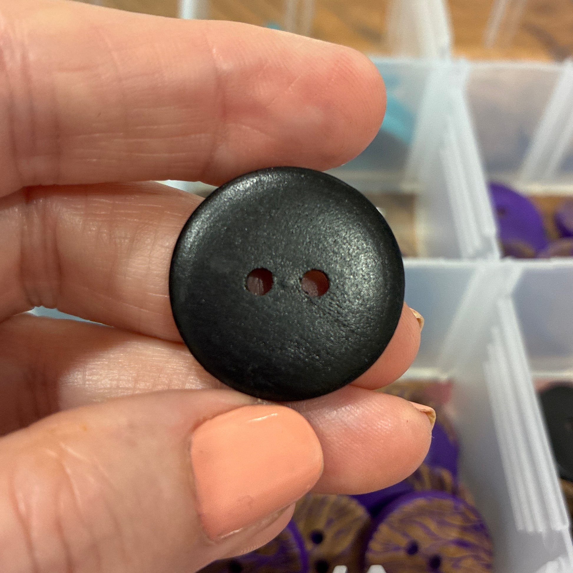 Black button held between fingers with a container of buttons in the background
