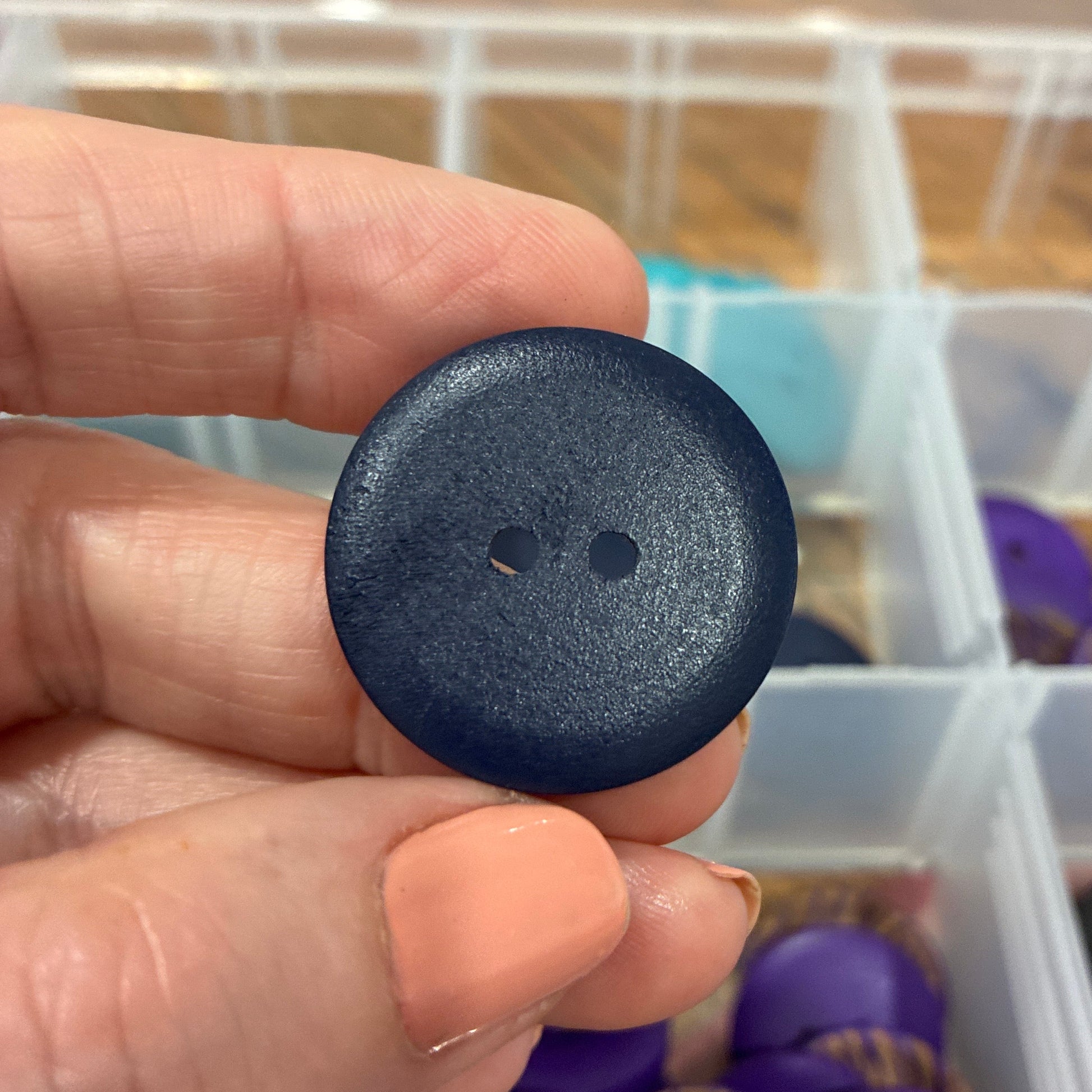Hand holding a black button with a container of buttons in the background