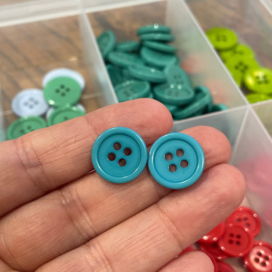 Hand holding two blue buttons with a container of assorted buttons in the background