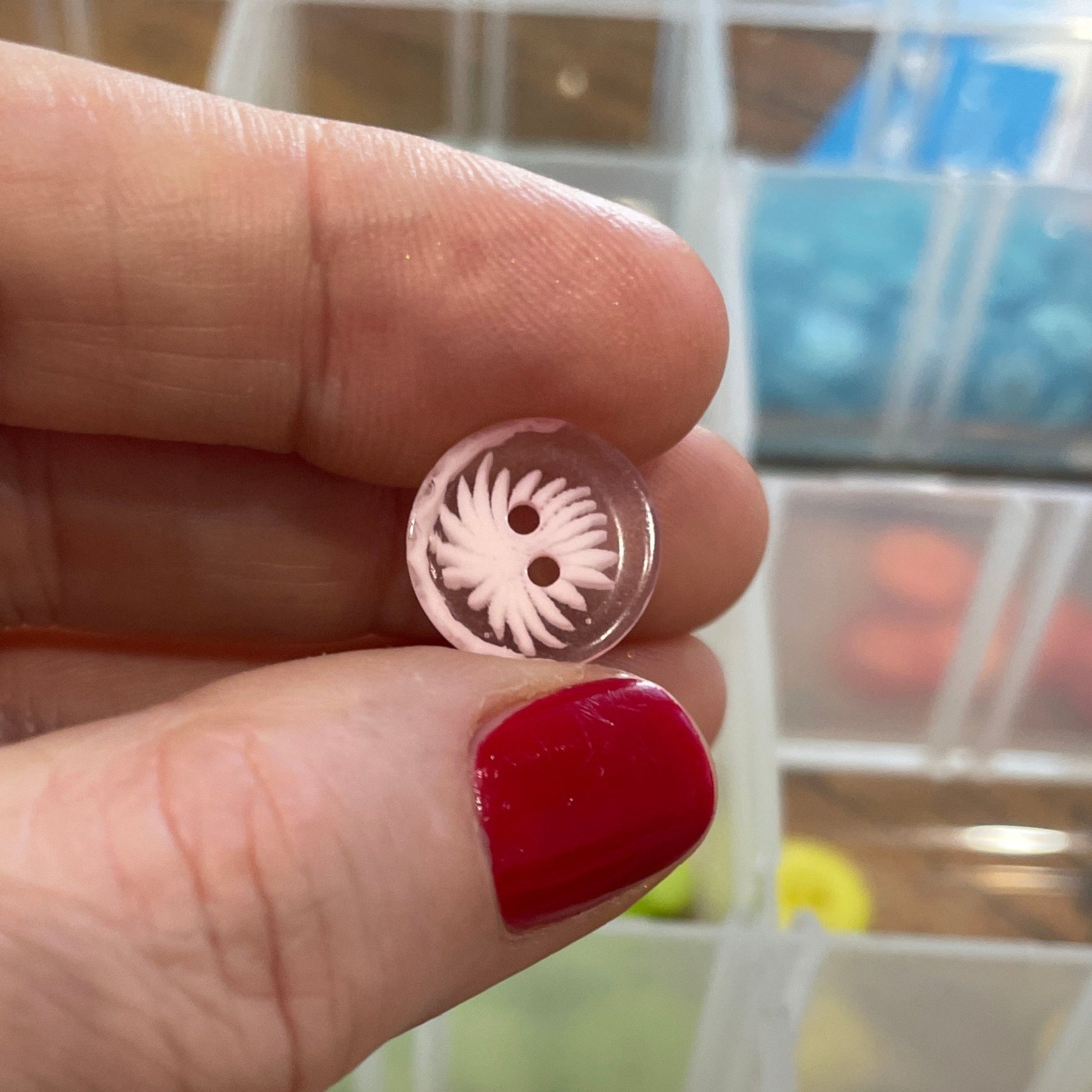 Hand holding a small metal object with a blurred background of a container with buttons.