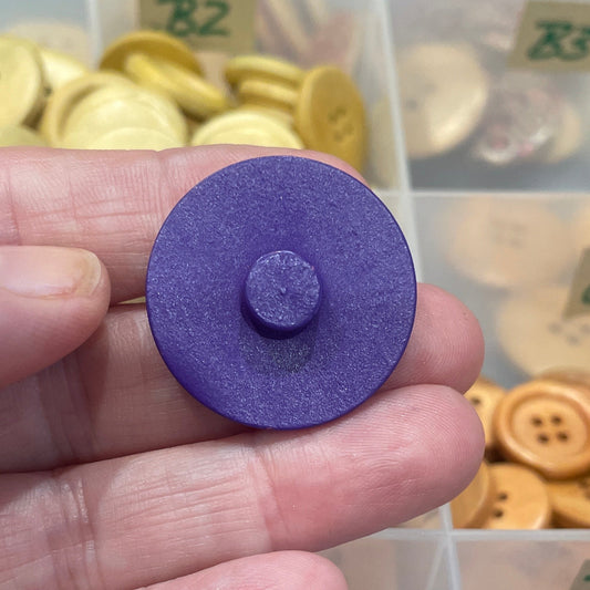 Hand holding a purple button with a container of buttons in the background