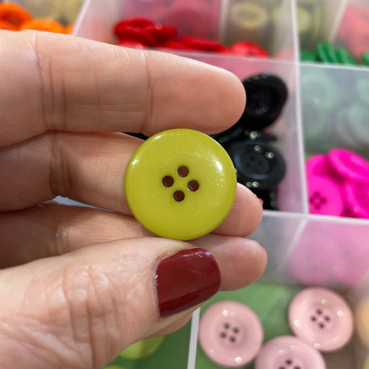 Hand holding a yellow button with a blurred background of assorted buttons
