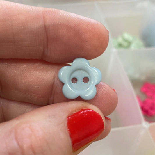 Hand holding a white flower-shaped button with a blurred background of colorful buttons.