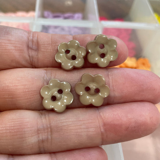 Three flower-shaped buttons held between fingers with a blurred background
