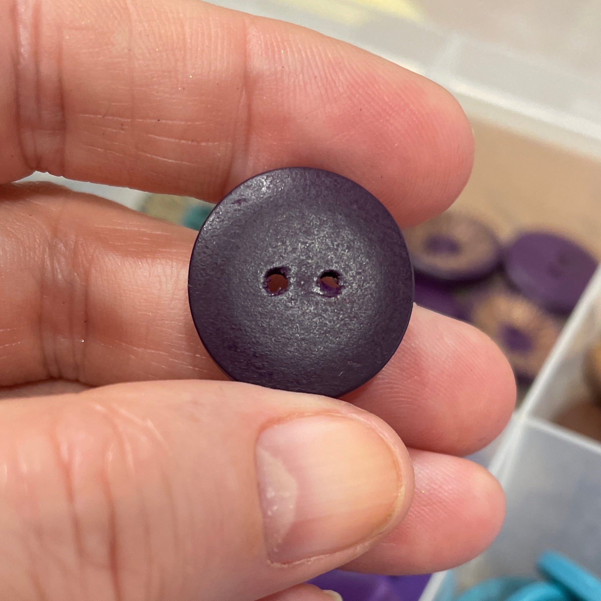 Hand holding a purple button with a container of buttons in the background