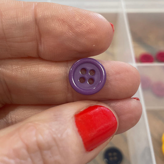 Hand holding a purple button with a clear container of buttons in the background