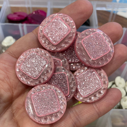 Hand holding pink glittery buttons with a container of yellow buttons in the background.