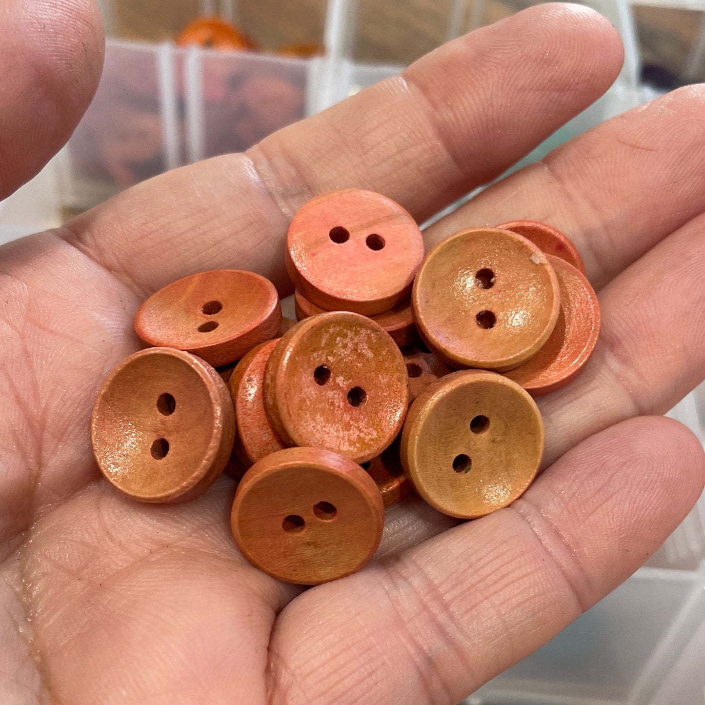 Hand holding small orange buttons with a container of buttons in the background