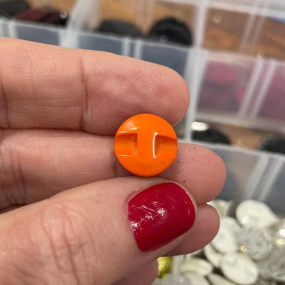 Hand holding an orange button with a blurred container of buttons in the background