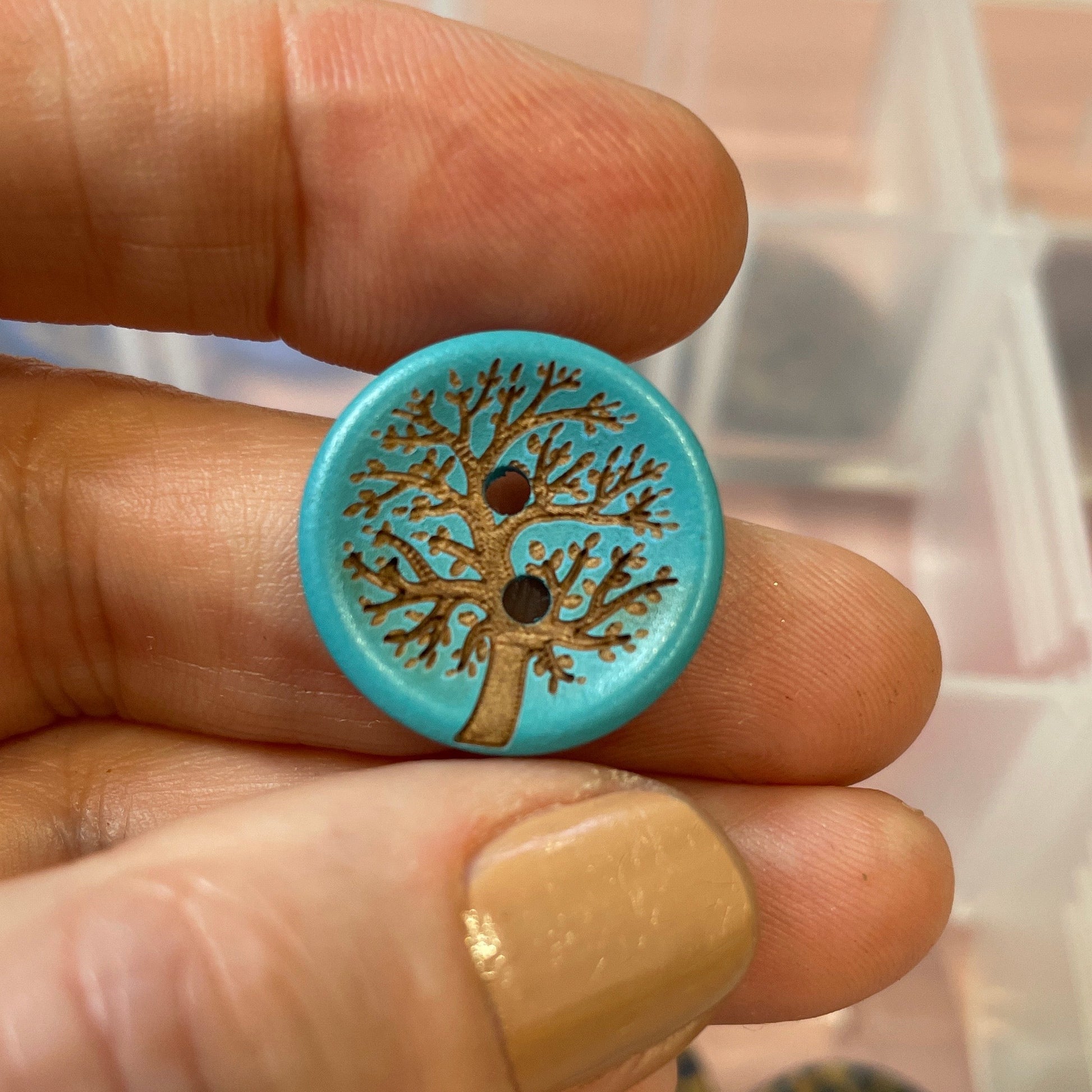 Hand holding a blue button with a tree design against a background of a clear container with buttons.