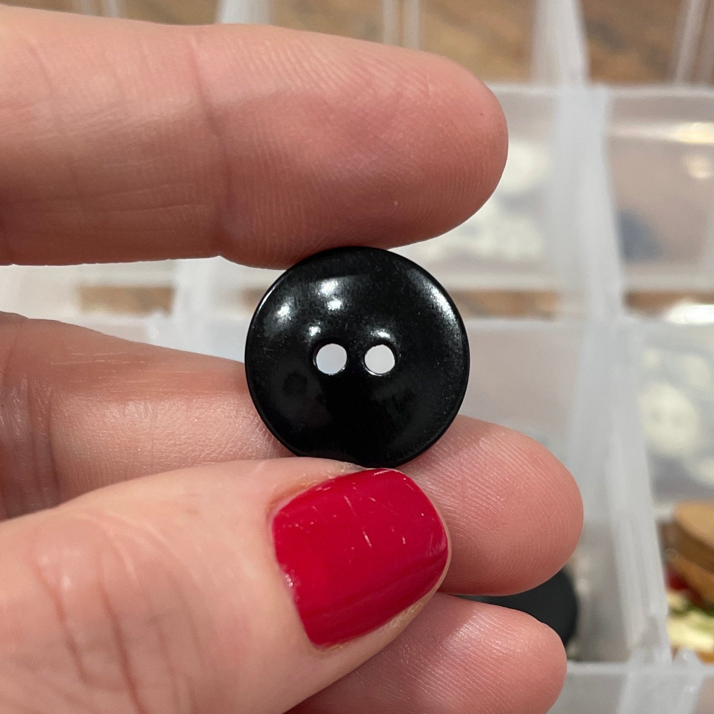 Person holding a black button with a clear container of buttons in the background