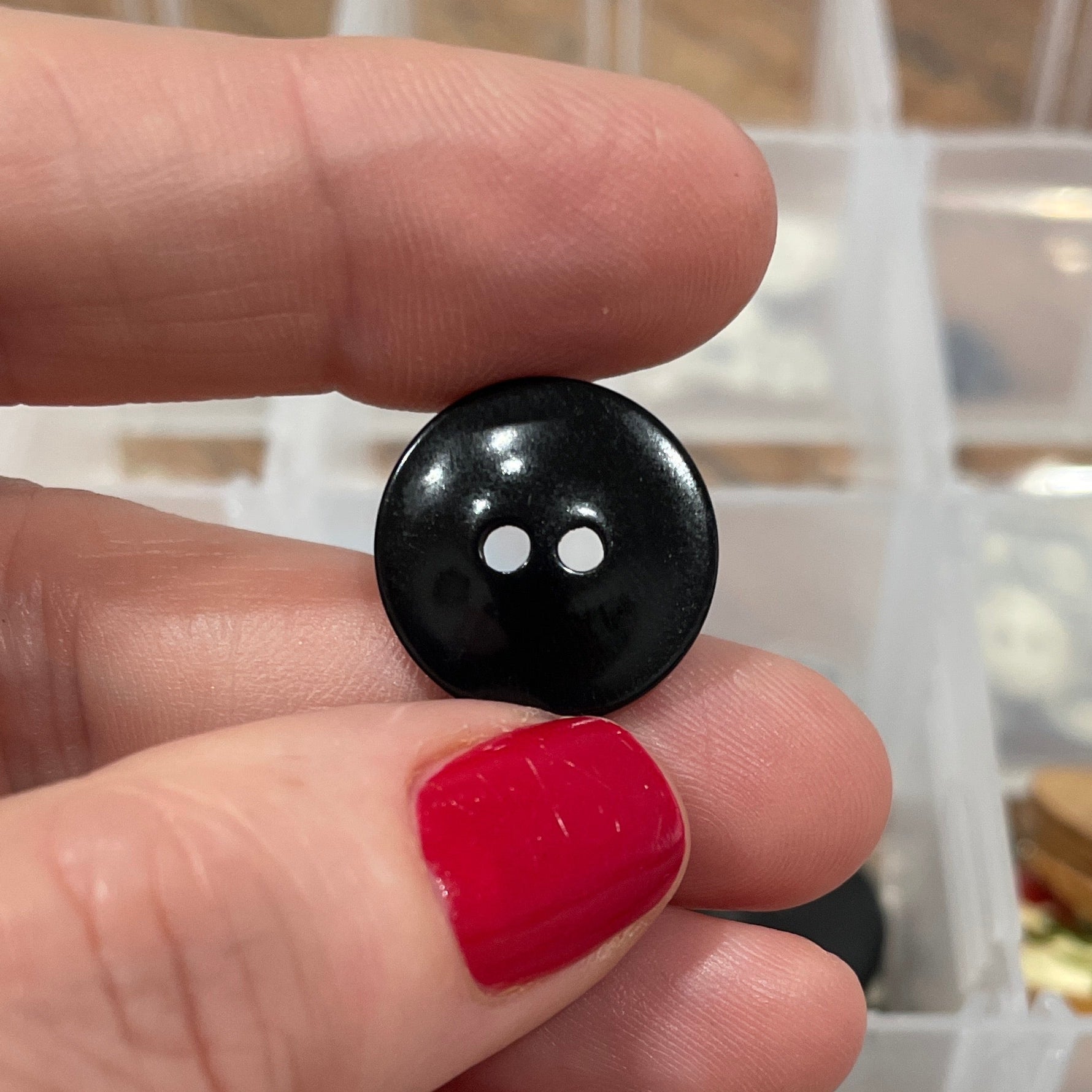 Person holding a black button with a clear container of buttons in the background