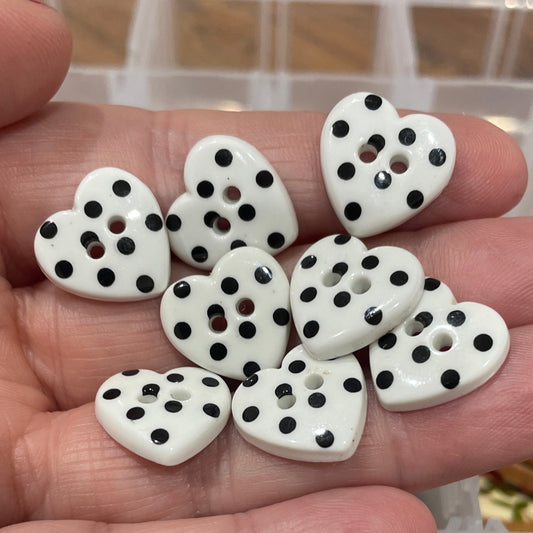 Hand holding white buttons with black dots in front of a container of assorted buttons.