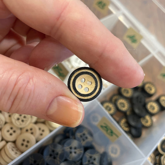 Hand holding a button with a background of various buttons in a container