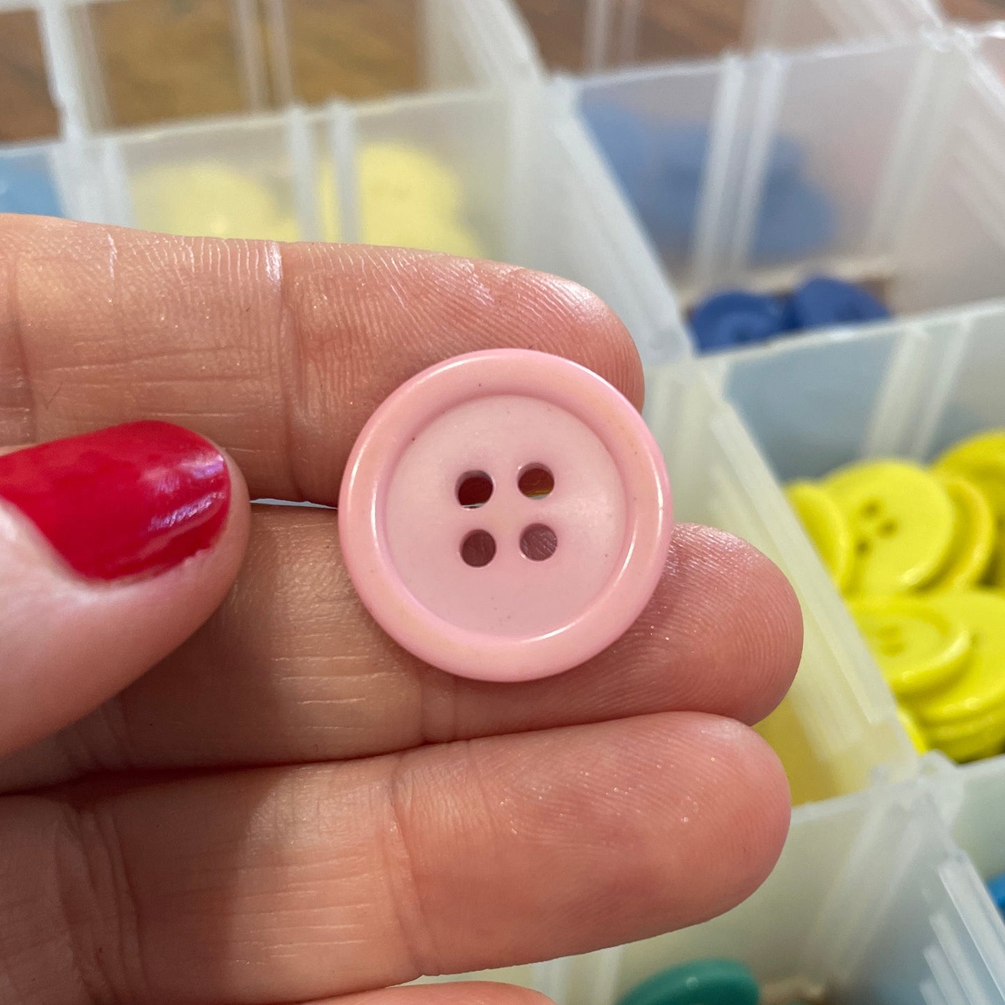 Pink button held between fingers with colorful buttons in the background
