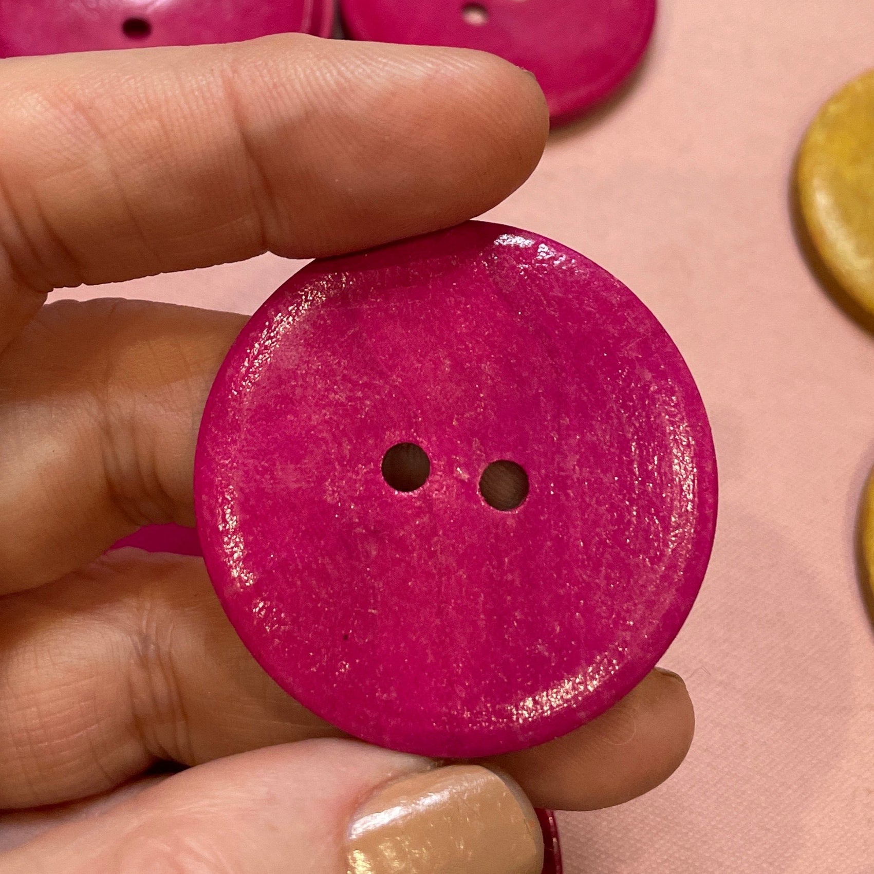 Hand holding a pink button with other buttons on a pink surface