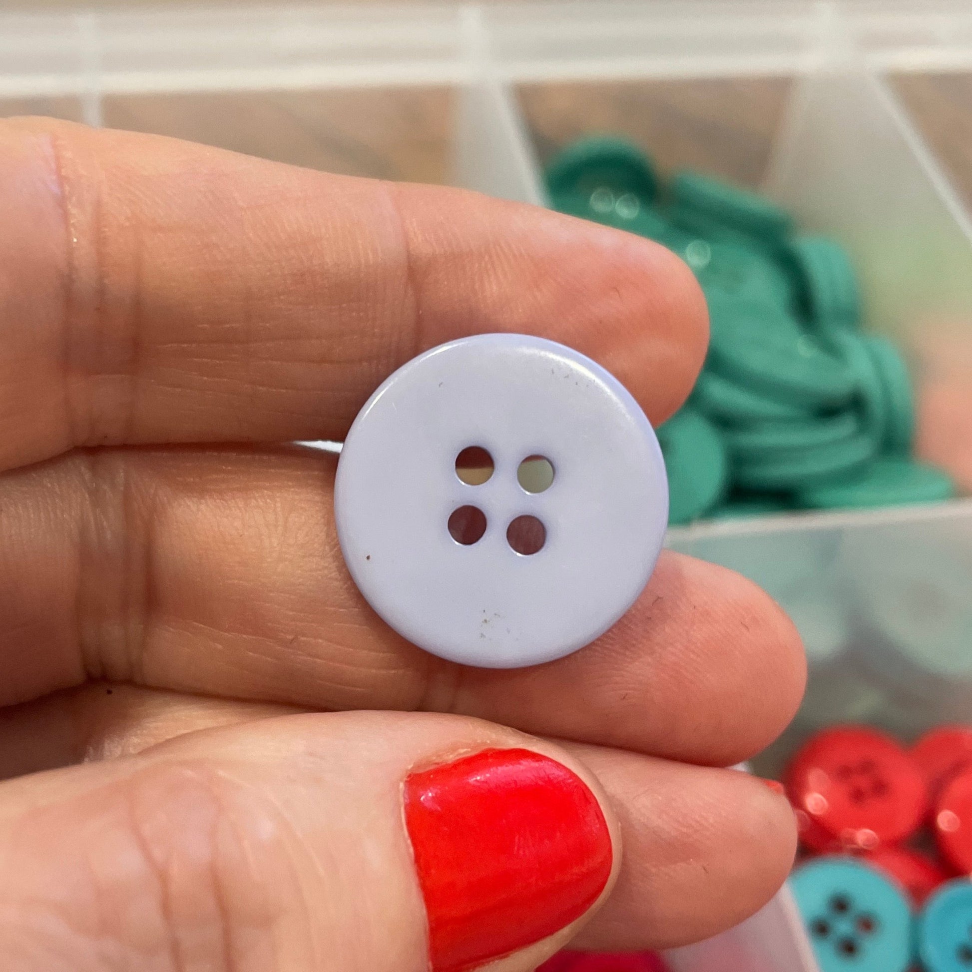 Hand holding a white button with a container of colorful buttons in the background