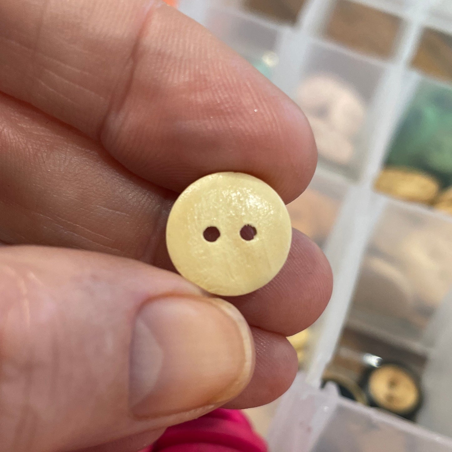 Hand holding a yellow button with a blurred background of assorted buttons in a container.