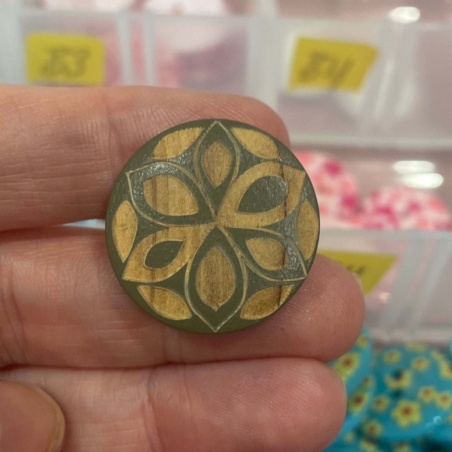 Hand holding a decorative button with a blurred background of button collection