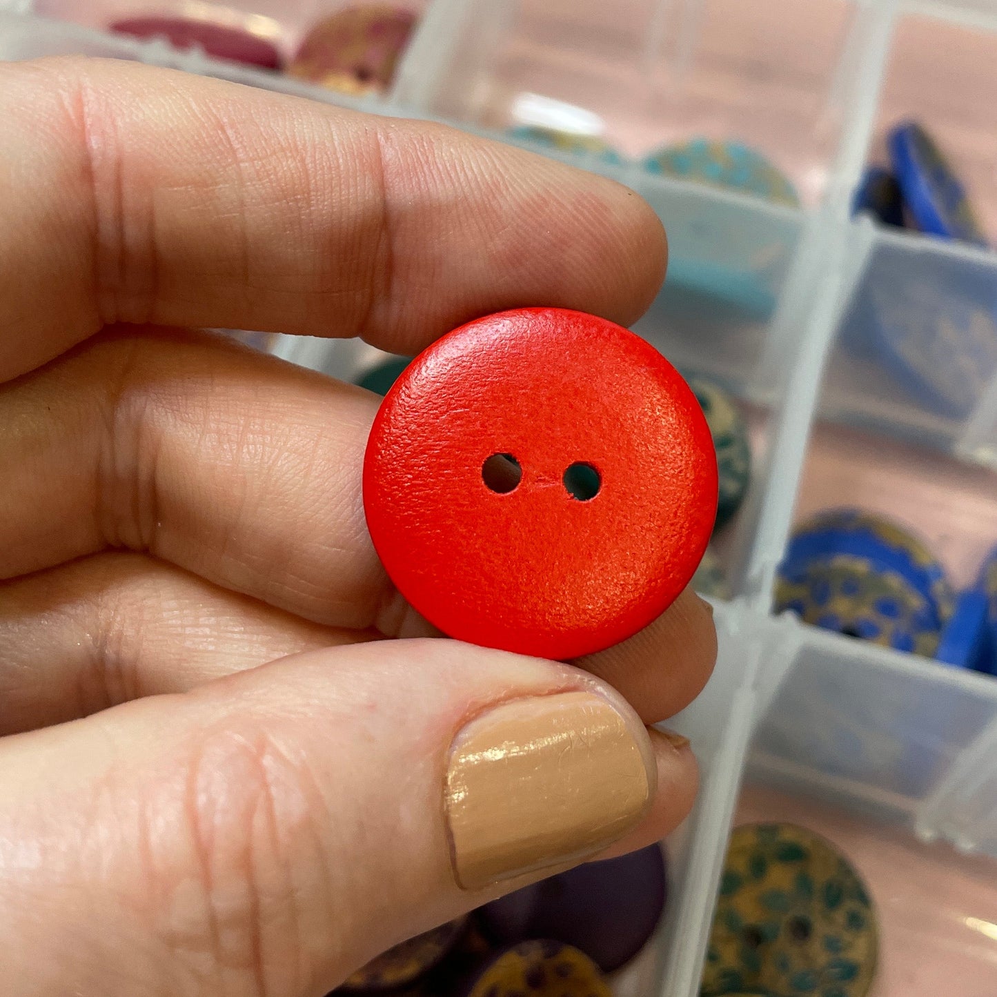 Hand holding a red button with a container of various buttons in the background