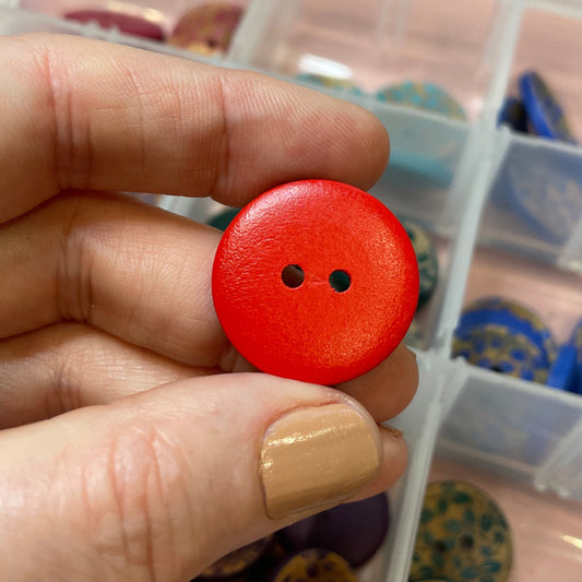 Hand holding a red button with a container of various buttons in the background