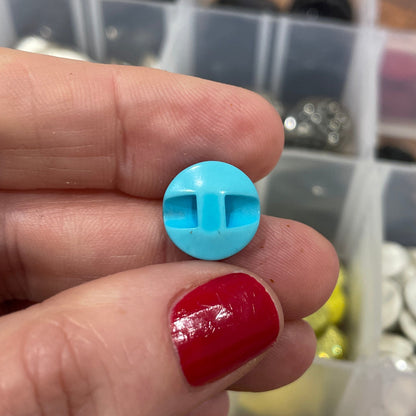 Hand holding two buttons, one blue and one red, with a container of buttons in the background.