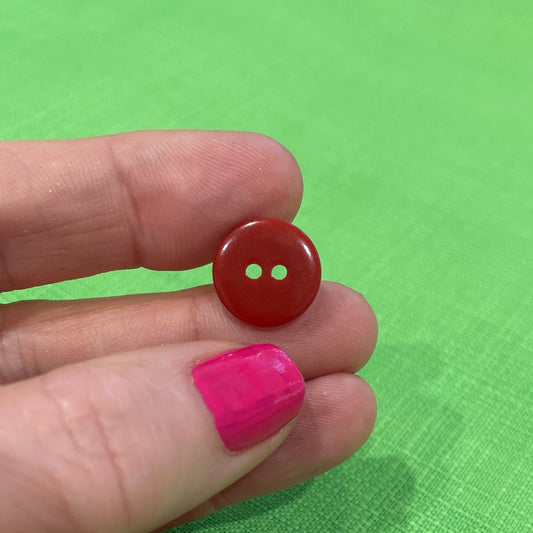 Red button held between fingers against a green background
