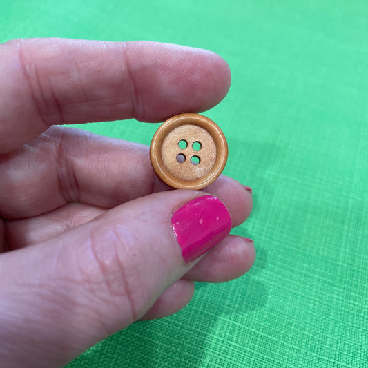 Wooden button held between fingers against a green background