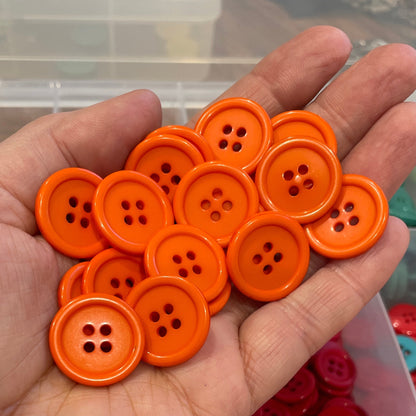 Hand holding orange buttons with a container of colorful buttons in the background